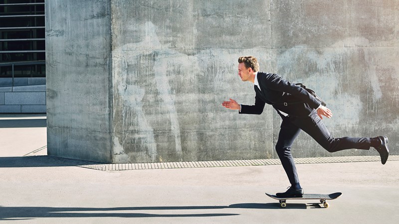 Man i kostym på skateboard.